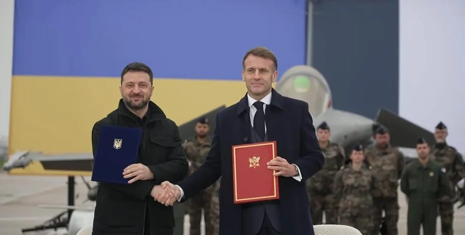 Емманюель Макрон і Володимир Зеленський тиснуть руки з документами перед прапором України та винищувачами