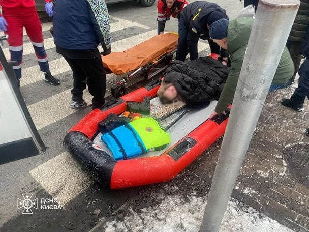 Медики на носилках переносять травмованого киянина через лід на засніженій вулиці