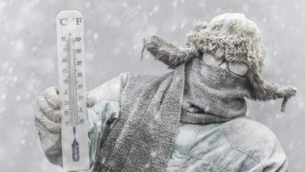 Чоловік у ушанці тримає термометр -28°C під снігопадом в Україні