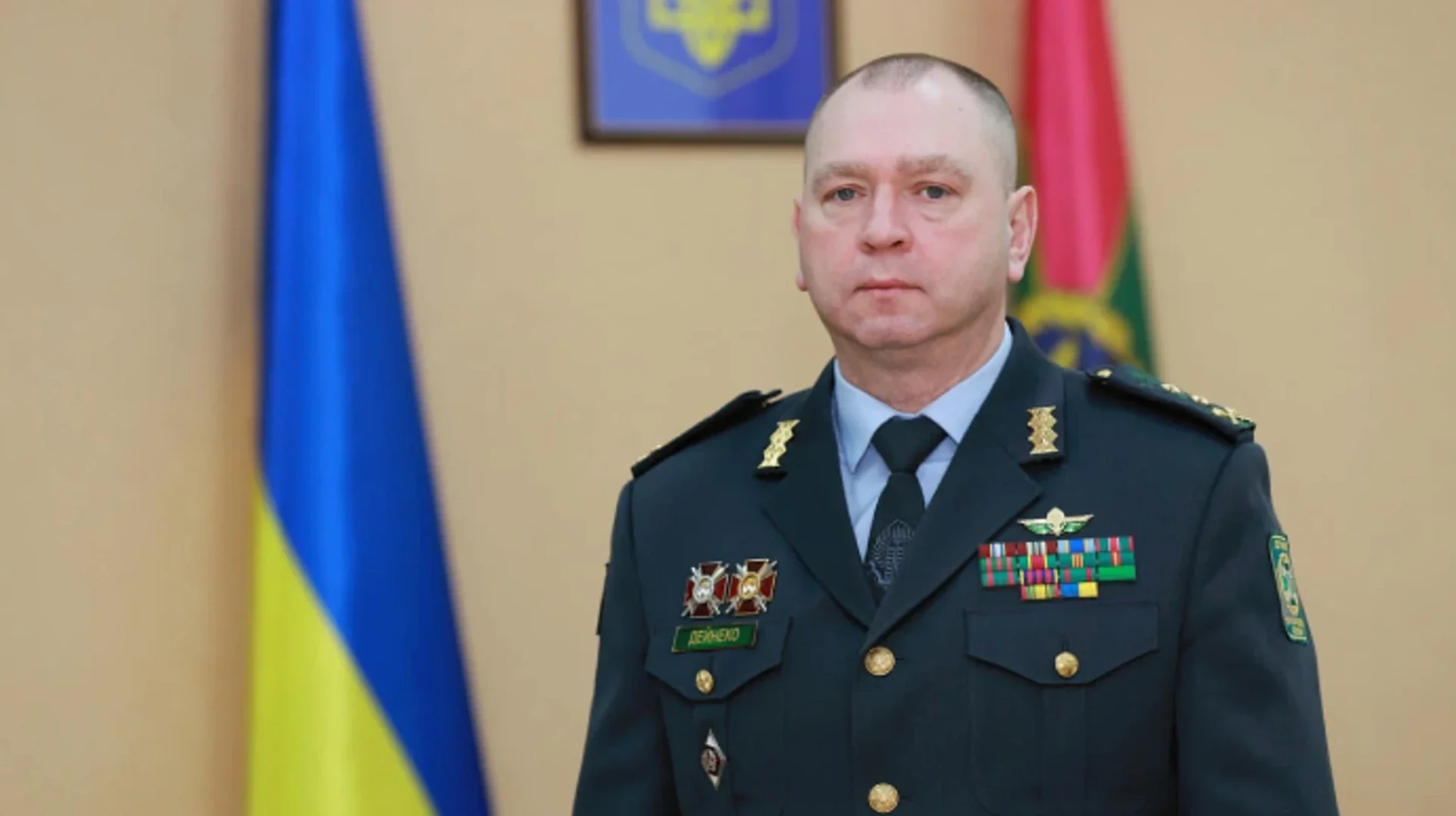 Сергій Дейнека, ексголова ДПСУ, у формі прикордонника на тлі прапорів