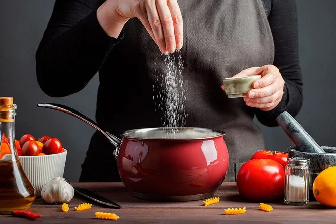 Повариха досыпает соль в бульон посреди варки для идеального вкуса