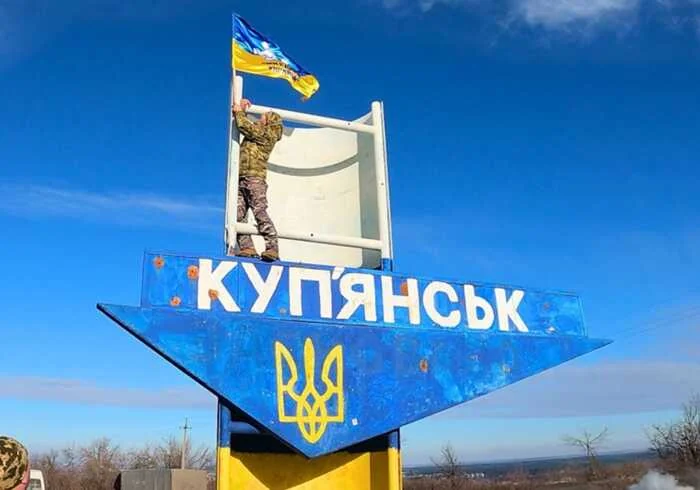 Військовий ЗСУ піднімає прапор над дорожнім знаком Куп’янськ на Харківщині
