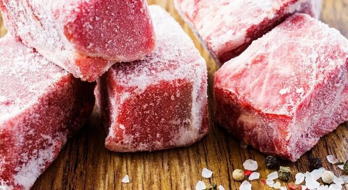 Замороженные куски мяса на доске с солью и перцем для варки или жарки