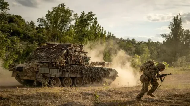 Російський танк із піхотою наступає на фронті, піднімаючи пил у лісі