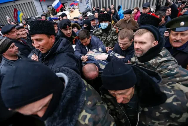 Российские оккупанты с флагами РФ окружают мужчину во время захвата Славянска.