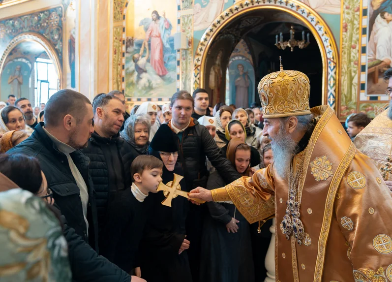 Патріарх Філарет у золотих облаченнях благословляє хлопчика хрестом у храмі серед вірян