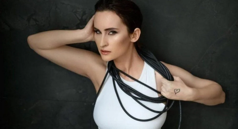 Катерина Павленко у драматичній позі з чорними ременями на білому топі