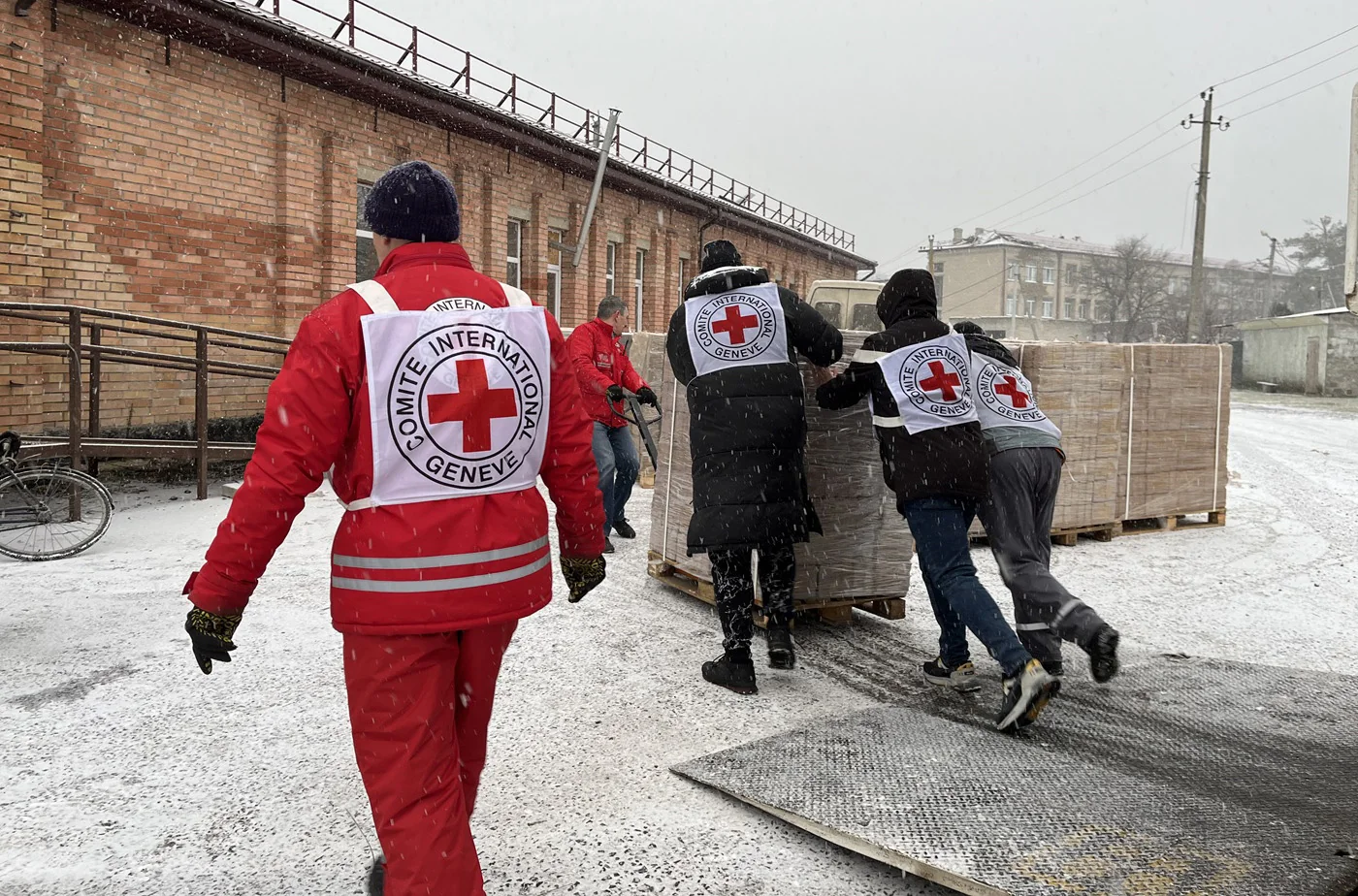 Працівники МКЧХ у жилетах з червоним хрестом несуть ящики допомоги на снігу в Україні