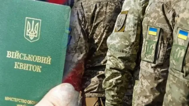 Військовий квиток України тримають біля військовослужбовців у камуфляжі під час мобілізації.