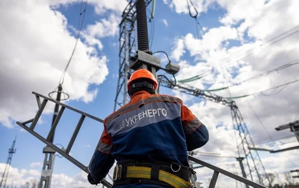 Працівник Укренерго ремонтує електроопори під хмарним небом через відключення світла в регіонах