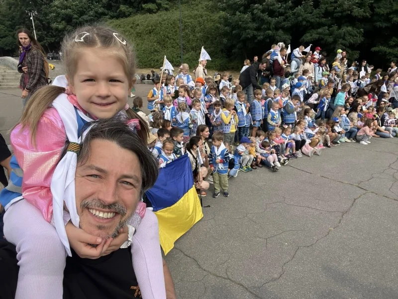 Сергій Притула тримає на руках 8-річну Соломію серед пластунов з прапорами.