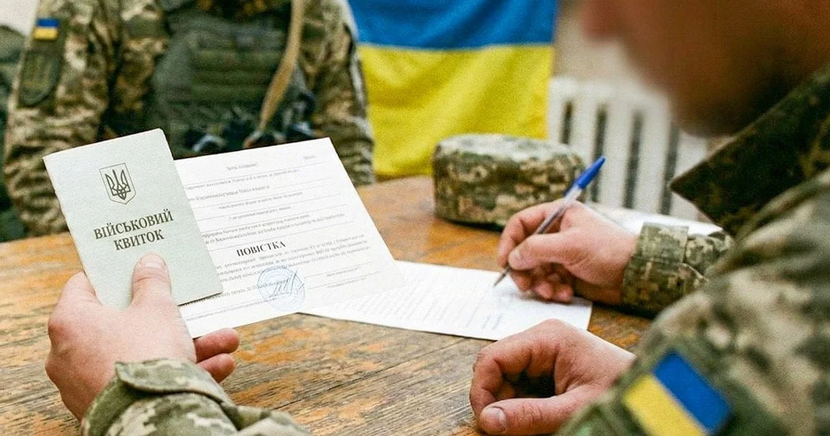 Представники ТЦК перевіряють паспорт громадянина України за столом з прапором.