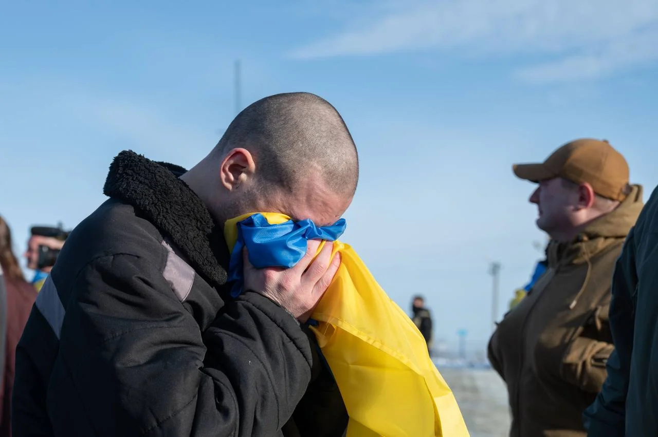 Звільнений з полону Назар Далецький ховає обличчя прапором України від сліз на кордоні