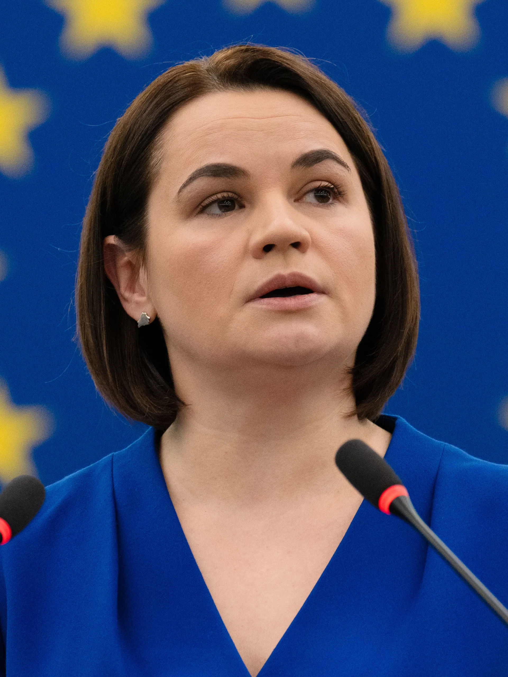Світлана Тихановська виступає перед мікрофонами на тлі прапора ЄС