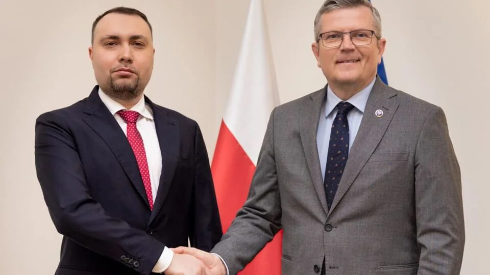 Український та польський посадовці тиснуть руки на тлі прапора Польщі