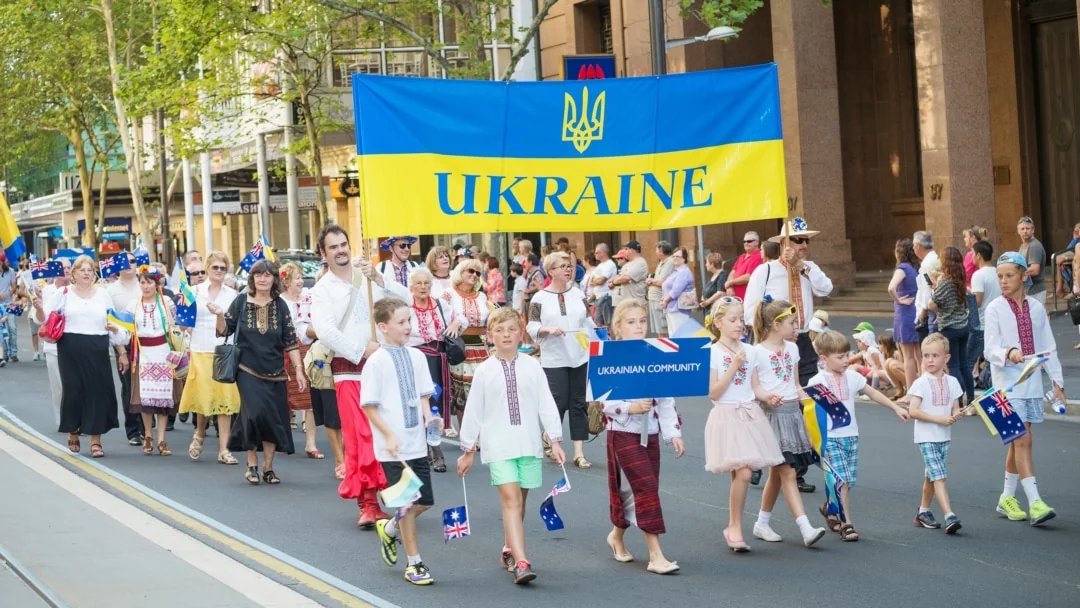 Українська діаспора на марші з прапором України та знаком громади
