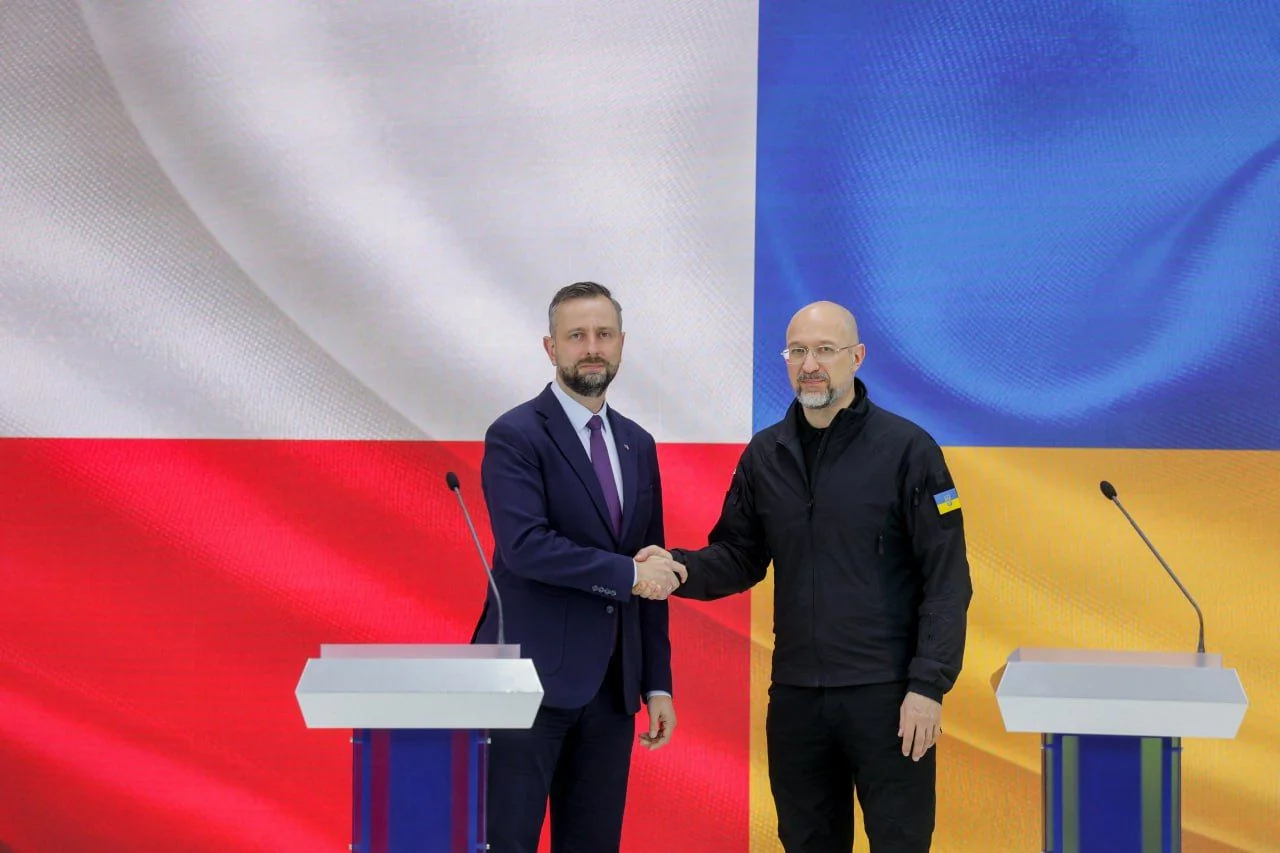 Косіняк-Камиш тисне руку українському представнику на тлі прапорів Польщі та України