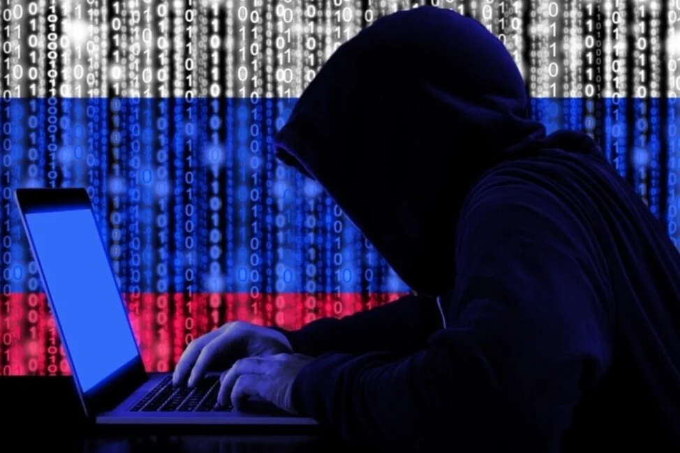 Хакер у капюшоні за ноутбуком на тлі прапора Росії та бінарного коду