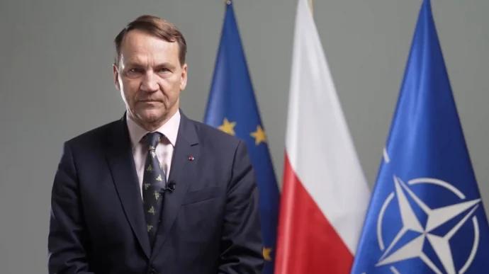 Радослав Сікорський на тлі прапорів ЄС, Польщі та НАТО
