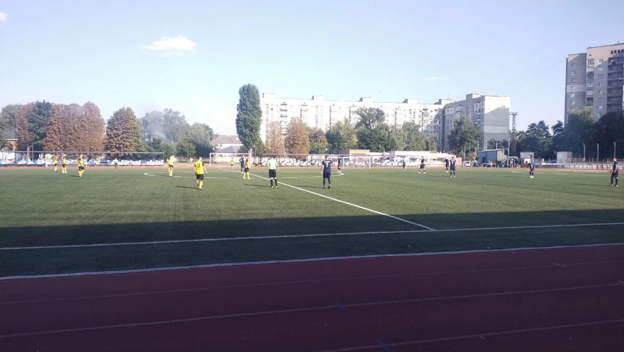 Футбольний матч на стадіоні з гравцями в жовтій і темній формі та багатоповерхівками