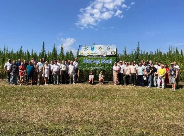 Група учасників Hemp Fest стоїть перед банером серед поля високих конопель