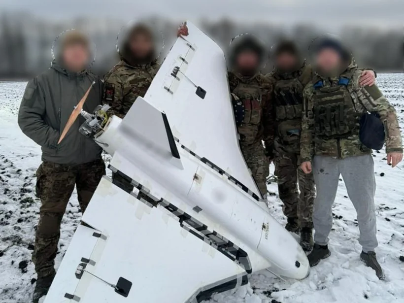 Пятеро військових у камуфляжі біля збитого білого дрона на сніговому полі