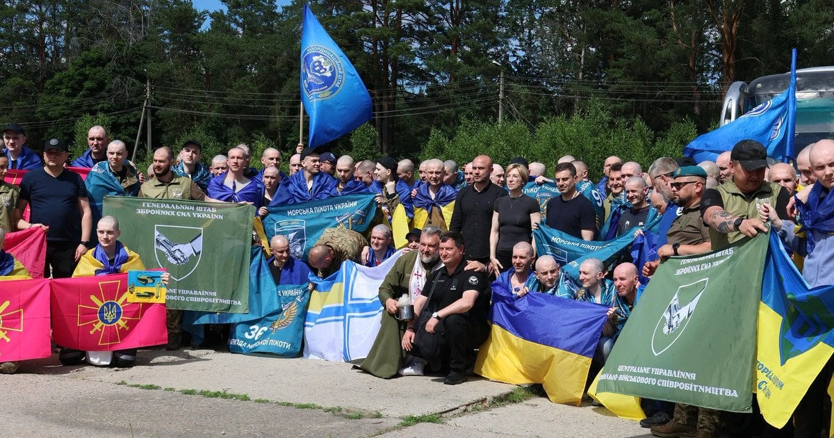 Звільнені українські військові з прапорами підрозділів зібралися біля лісу після обміну