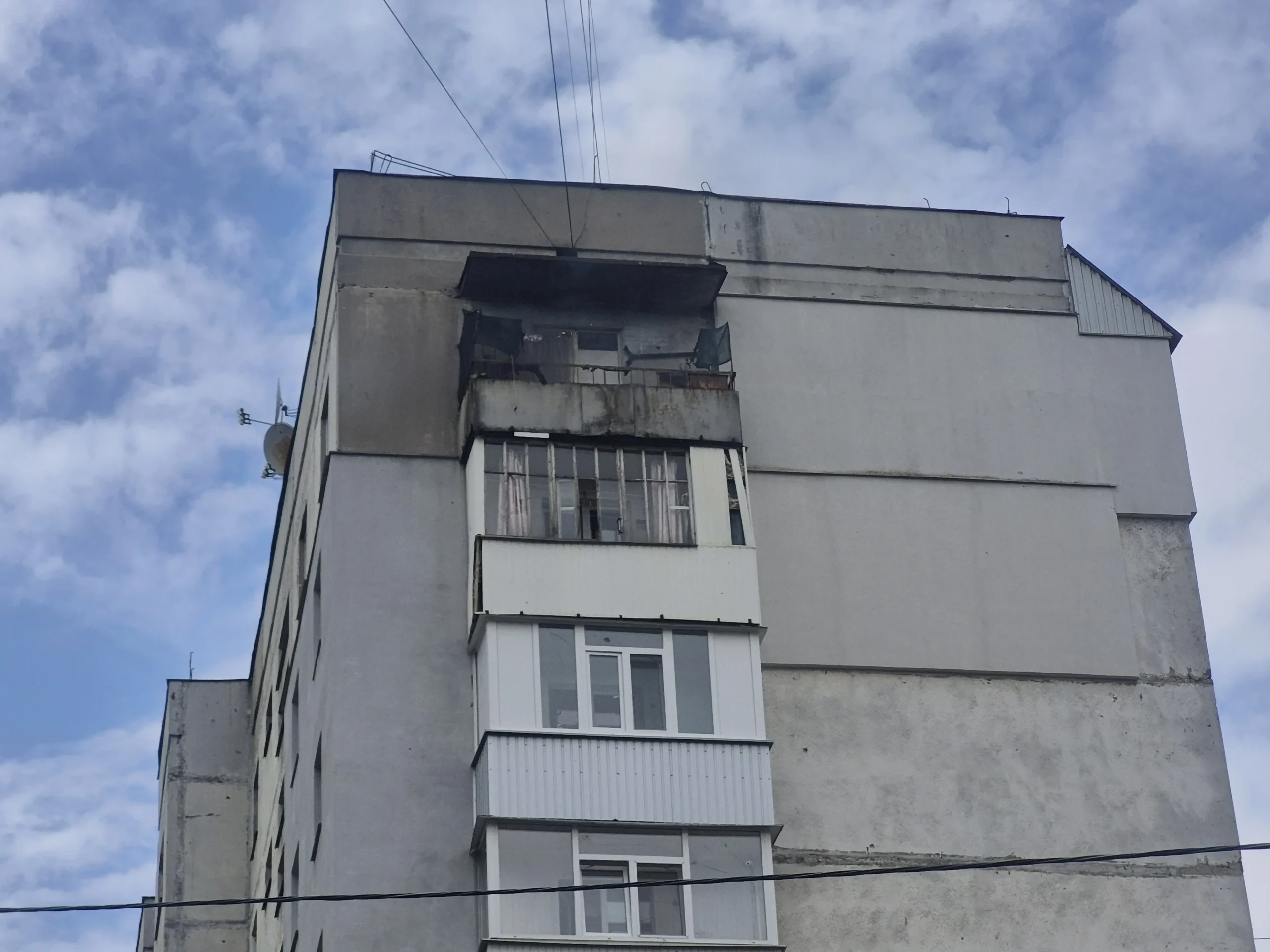 Сіра багатоповерхівка з заскленими балконами та пошкодженим верхнім ярусом