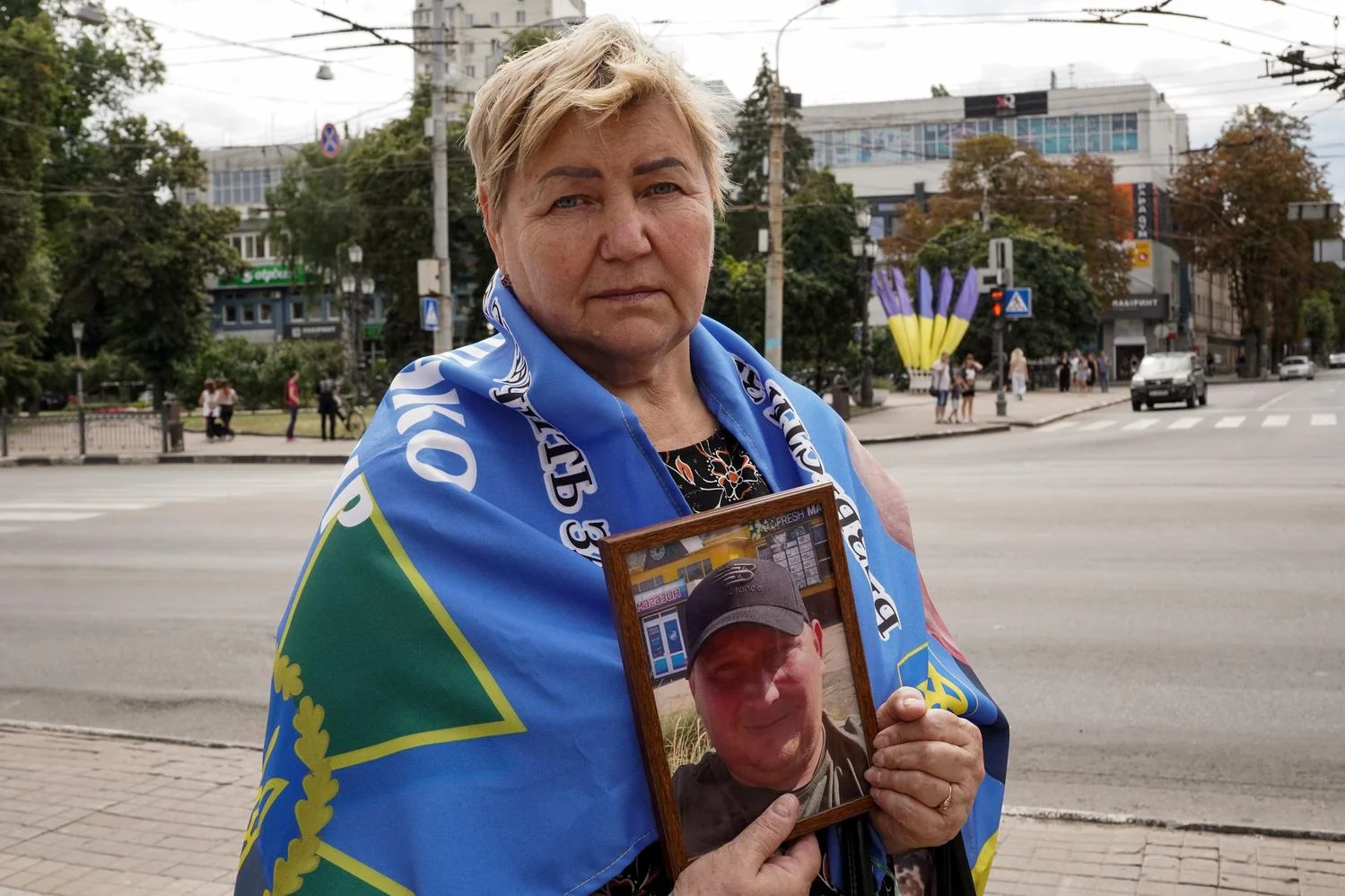 Жінка в синьому прапорі тримає портрет чоловіка на вулиці Сум