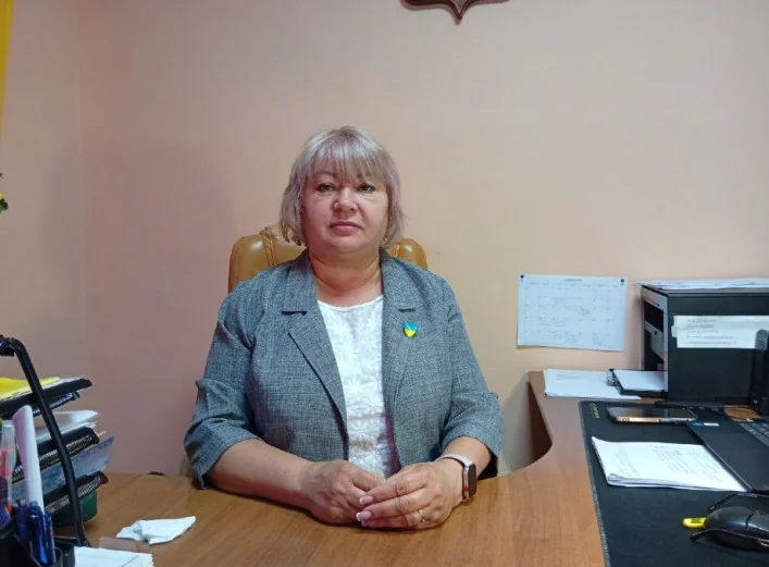 Жінка в сірому піджаку сидить за столом у кабінеті сільської ради