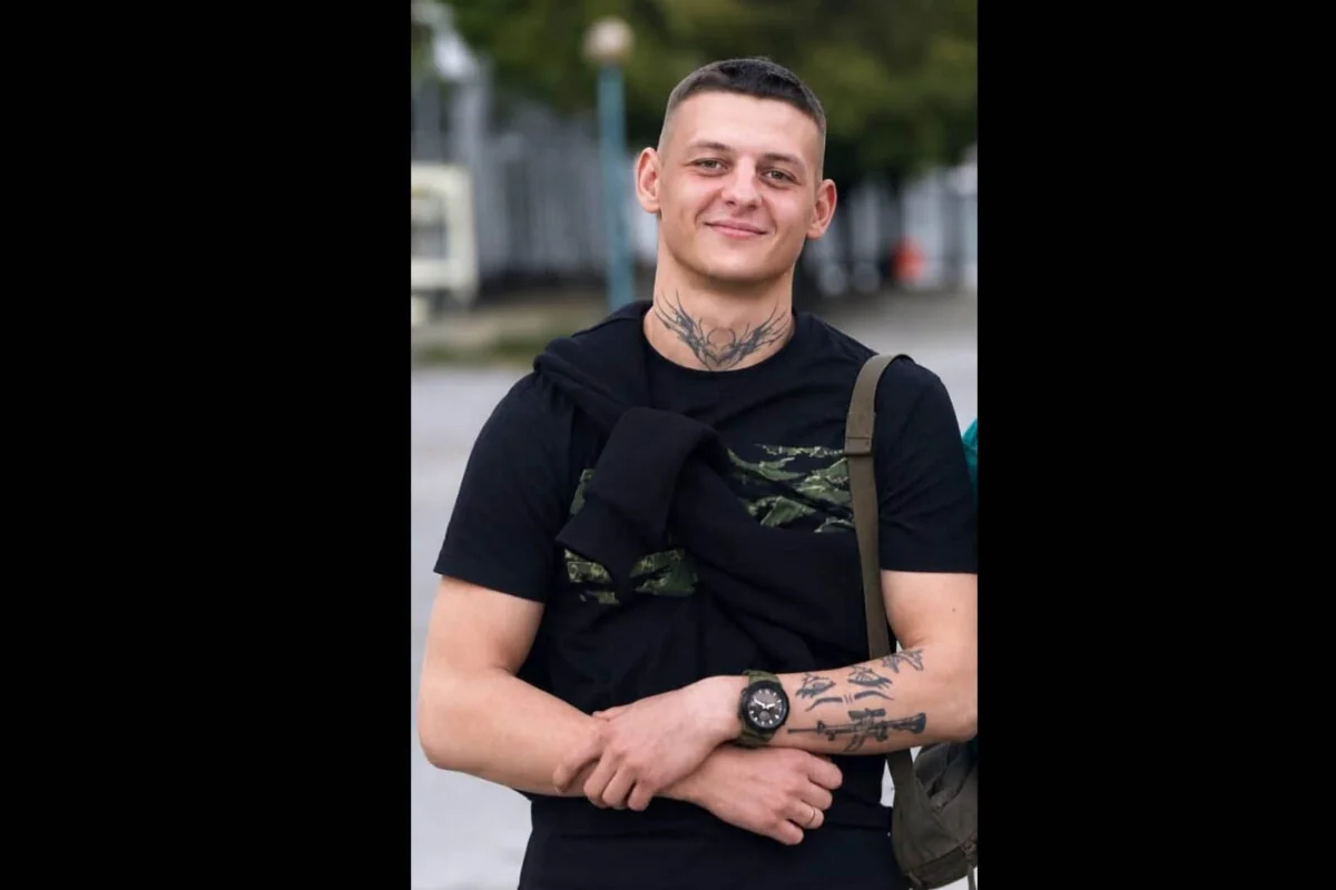 Усміхнений молодий чоловік з коротким волоссям і татуюванням на шиї в чорній футболці
