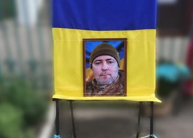 Меморіальний стенд з українським прапором і портретом чоловіка в шапці