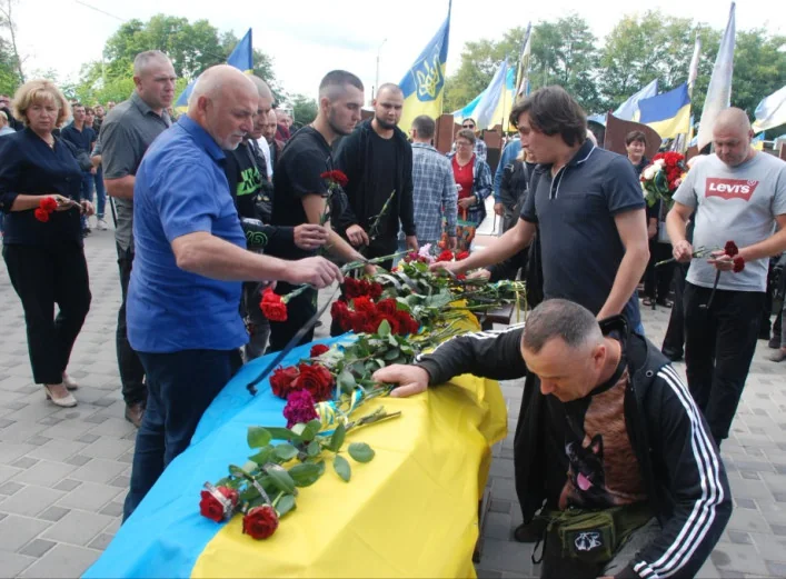 Люди кладуть червоні троянди на труну, накриту українським прапором
