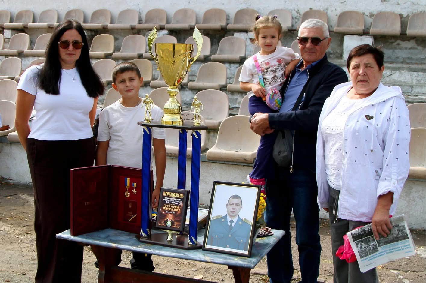 Родина біля кубка, медалей і портрета Героя Івашка на стадіоні Кролевця