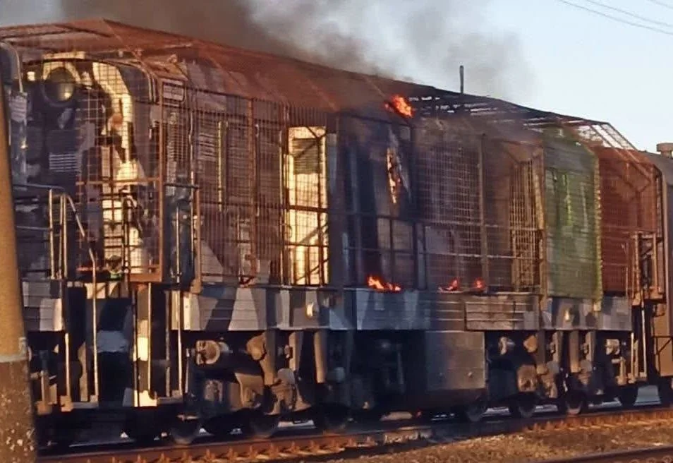 Горіючий локомотив з металевими ґратами, полум’ям і димом на залізничних коліях