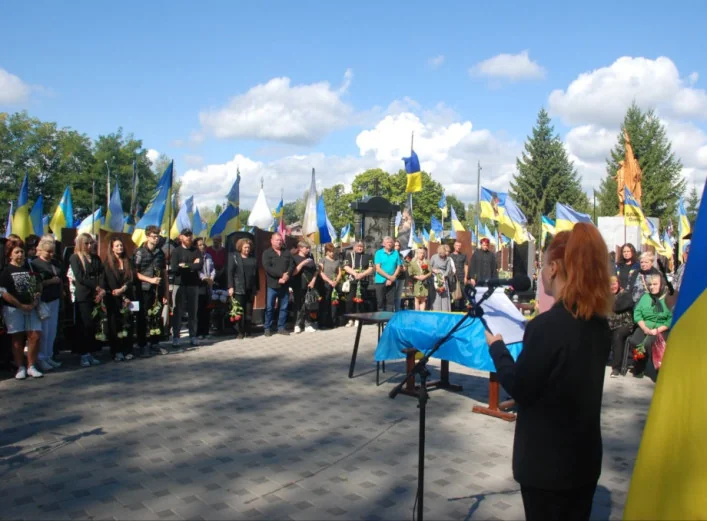 Церемонія прощання на кладовищі: люди з прапорами слухають промову біля мікрофона