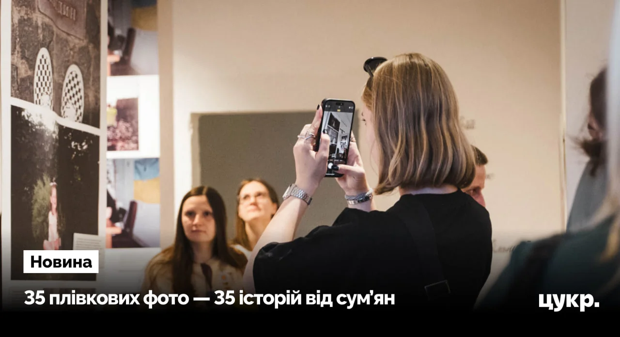 Жінка фотографує смартфоном світлини на стіні виставки, відвідувачі дивляться